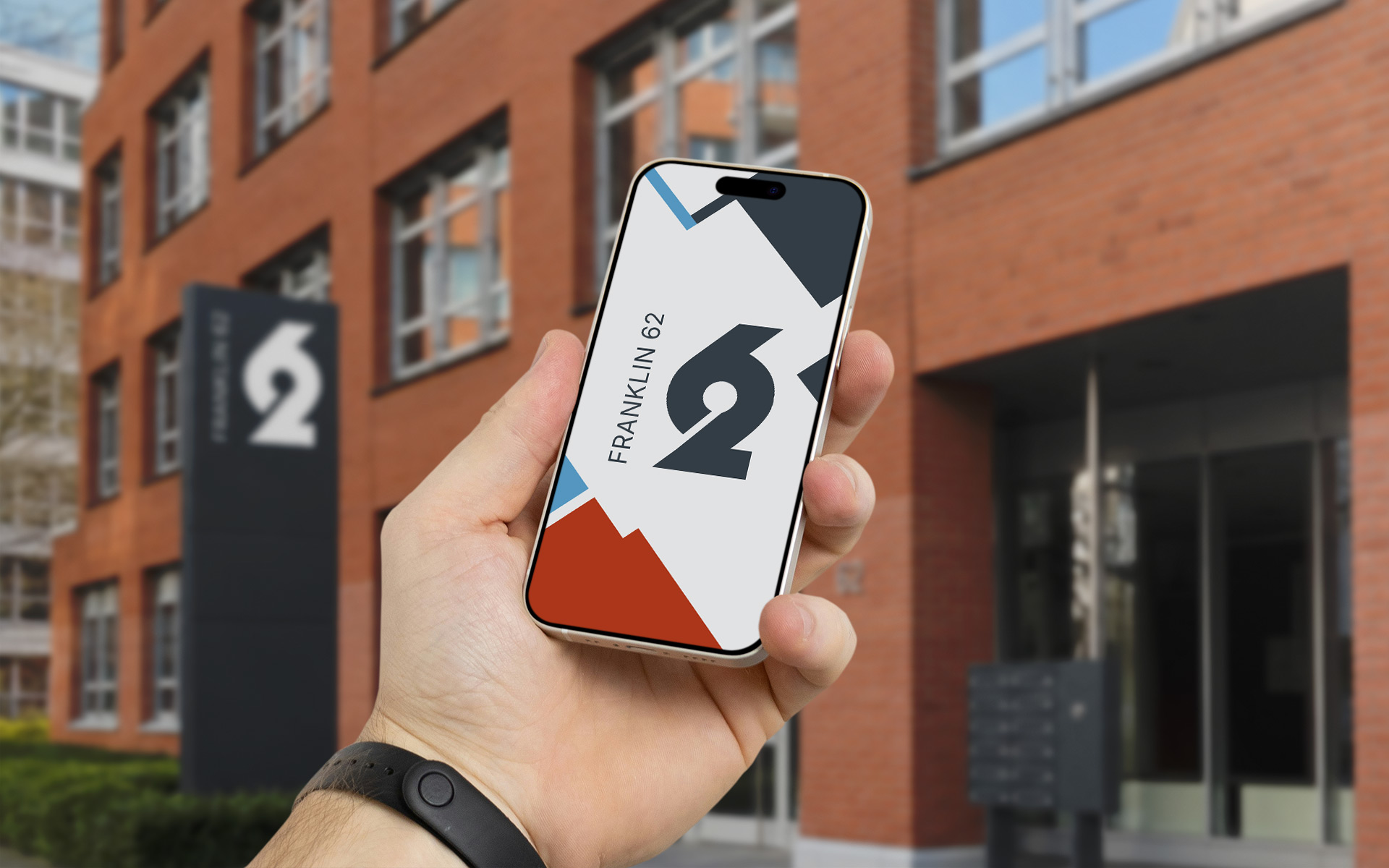 Hand hält vor dem Bürogebäude Franklin 62 in Frankfurt ein iphone. Auf dem Screen ist das Logo sowie das Keyvisual vom Franklin 62zu sehen.